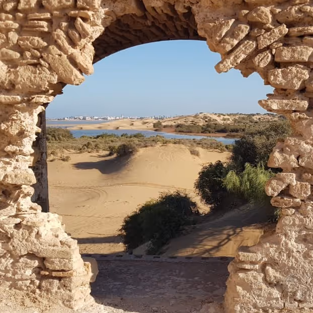 Sand dunes and coastline seen through an ancient stone arch
