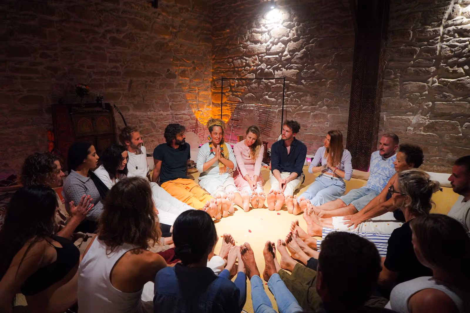 A meditation circle with participants seated barefoot around the light of candles
