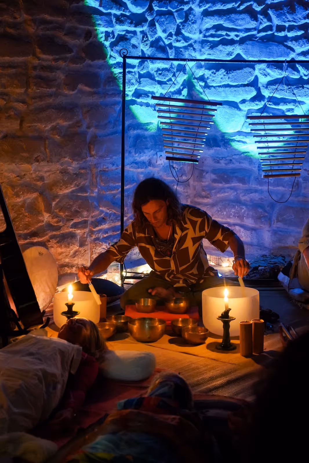 Morgan performing a sound bath with singing bowls in a stone-walled room lit in blue